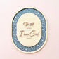 Oval wooden wall art featuring the carved text 'Best and know I am God Psalm 46:10' in rose-gold lettering, set against a glittery blue and white patterned background, displayed on a soft pink wall.