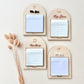Four arched wooden notepad holders arranged in a 2x2 grid on a light beige background, with dried grass stems along the left side. The holders have engraved names or labels: Mr.