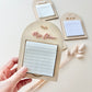 A hand holds a wooden arched notepad holder engraved with 'Mrs. Clara' in rose gold script, showing a white lined notepad inside.