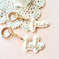 Two personalized acrylic keychains with gold-tone keyrings and clips, featuring the names 'frank' and 'kala' in white cursive script, styled on a pink background with a white lace doily.