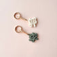 Two small metal keychains with Chinese character charms on a pale pink background. One charm is white and the other is dark green, both attached to rose gold keyrings.