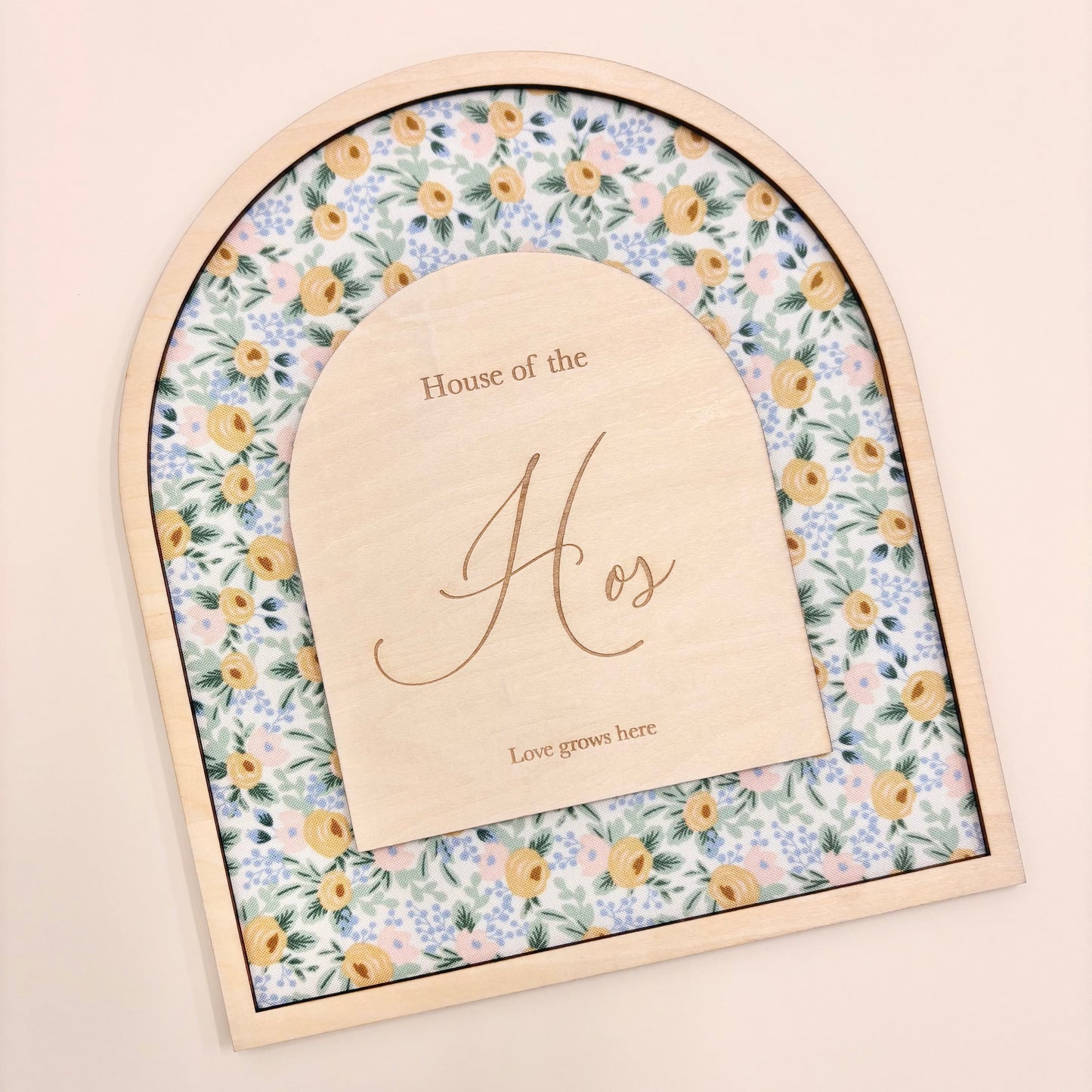 An arched wooden keepsake box or plaque with a floral patterned insert and a central wooden insert card engraved with 'House of the Hos' and 'Love goes here', shown on a plain beige background.