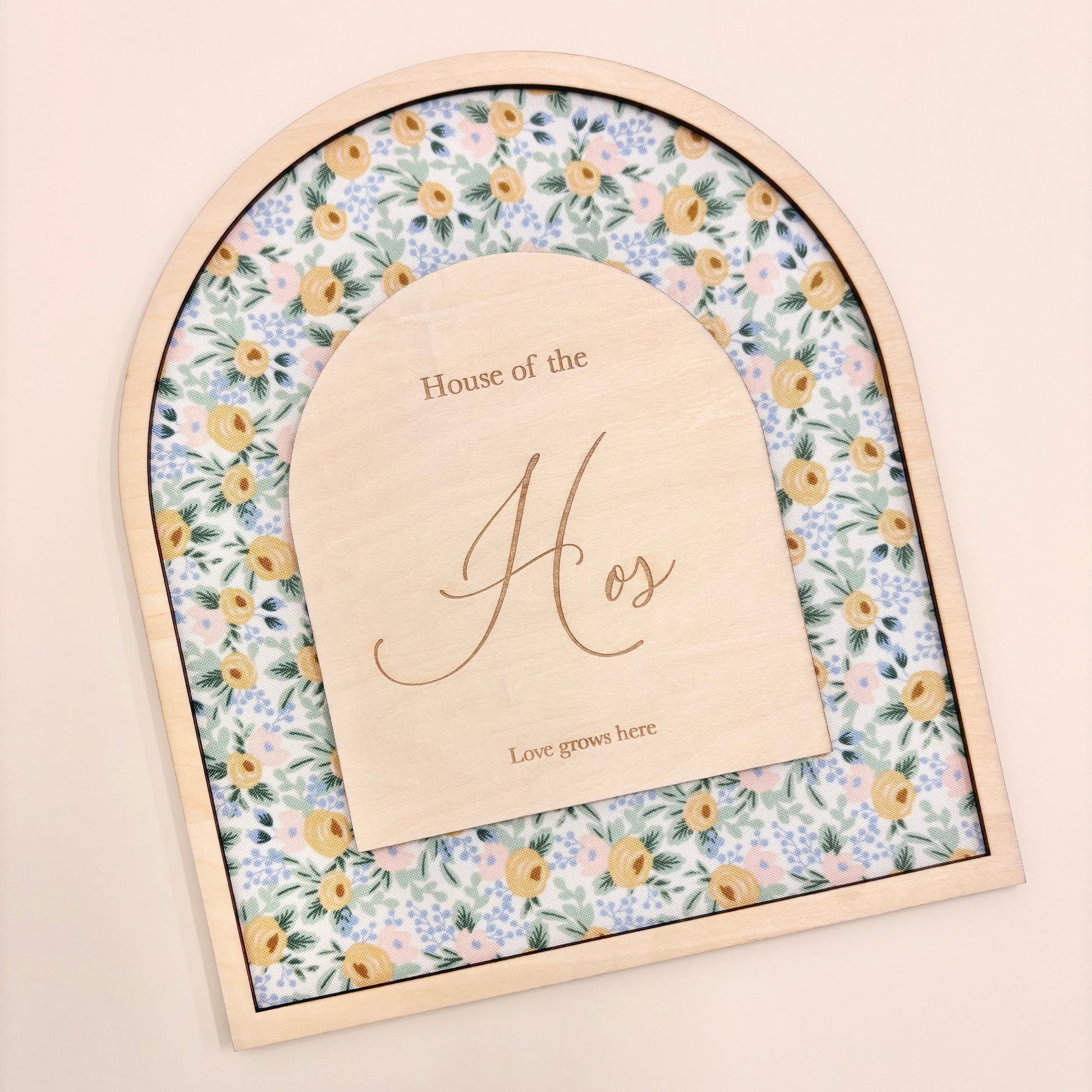 An arched wooden keepsake box or plaque with a floral patterned insert and a central wooden insert card engraved with 'House of the Hos' and 'Love goes here', shown on a plain beige background.