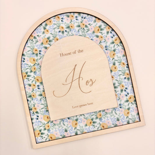 An arched wooden keepsake box or plaque with a floral patterned insert and a central wooden insert card engraved with 'House of the Hos' and 'Love goes here', shown on a plain beige background.