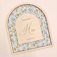 An arched wooden keepsake box or plaque with a floral patterned insert and a central wooden insert card engraved with 'House of the Hos' and 'Love goes here', shown on a plain beige background.