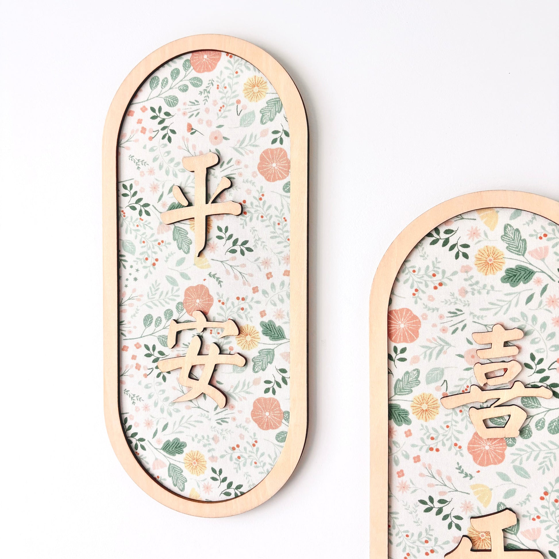 Two vertical oval wooden wall plaques with floral-patterned inserts and raised Chinese characters, shown against a clean white background.