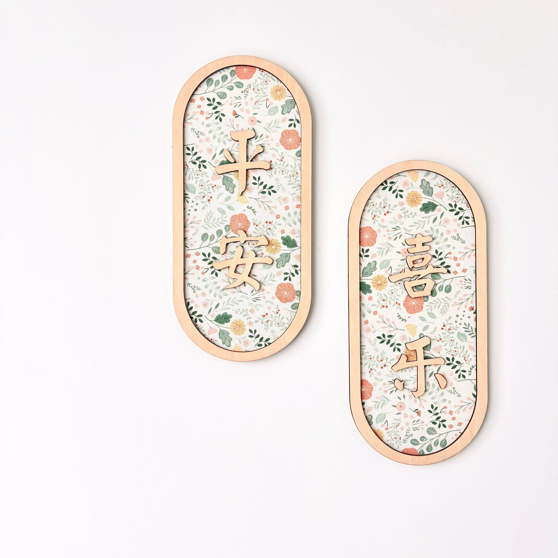 Two vertical oval wall decorations with light wood frames, featuring a delicate floral pattern and Chinese characters, displayed on a clean white background.