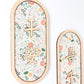 Two vertical oval wall decorations with light wood frames, featuring a delicate floral pattern in soft pink, orange, and green on a white background, with gold Chinese characters.
